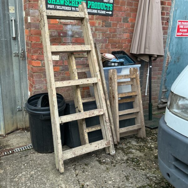 Three vintage wooden trestles leaning against a wall.