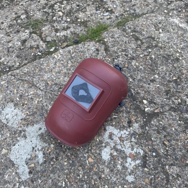 Front view of a used welders mask with clear screen.