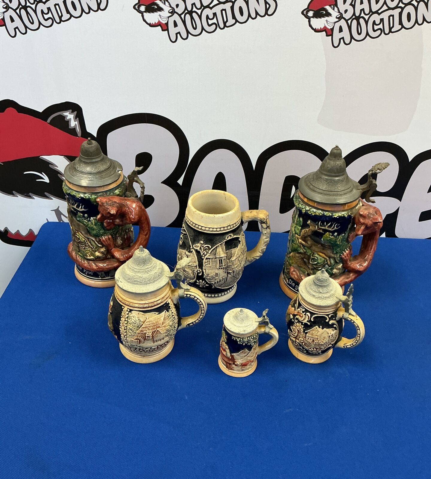 Lot of vintage West German beer steins with detailed ceramic designs.