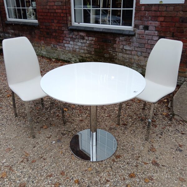 Modern white dining table and two chairs set in a home setting.