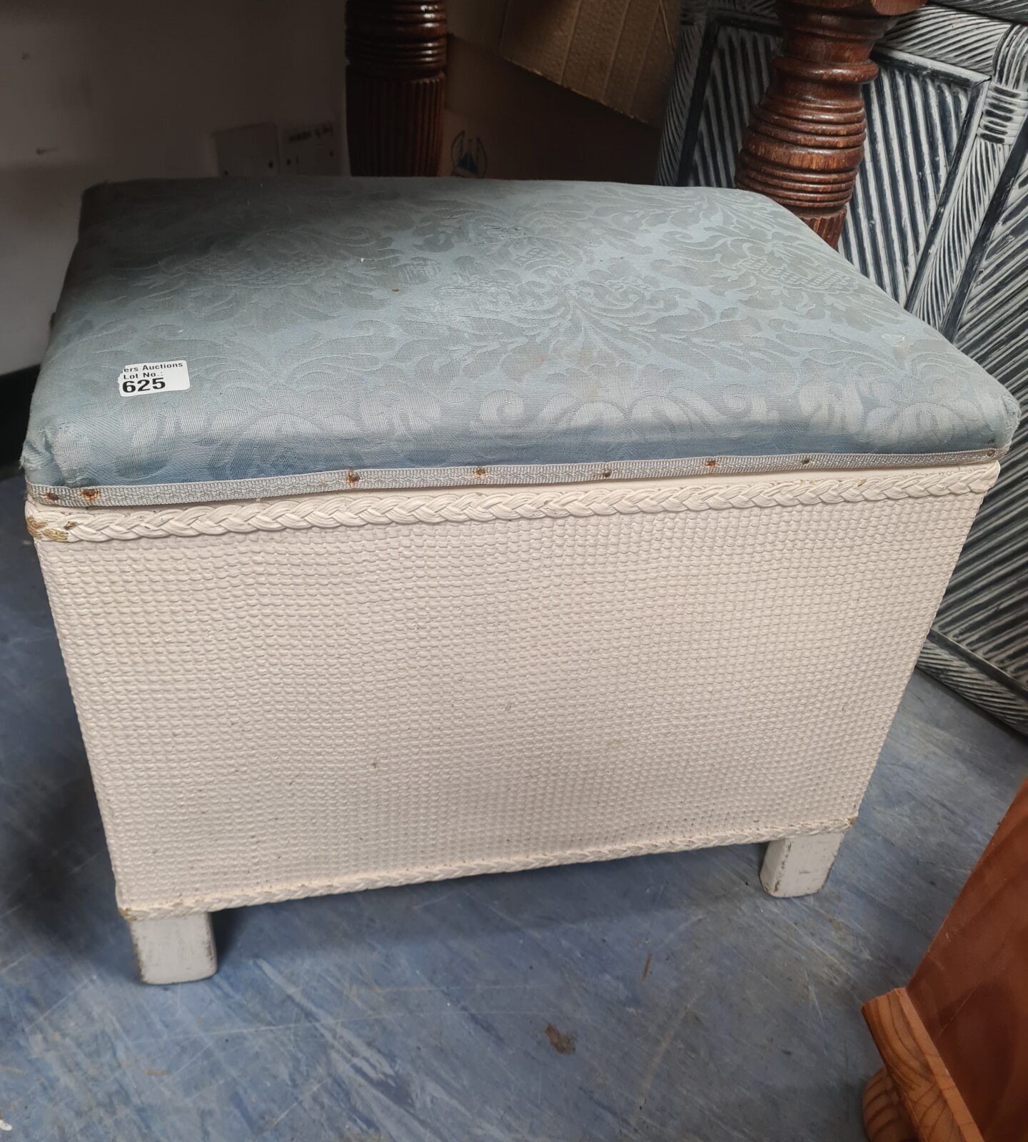 Vintage wicker footstool with blue patterned cushion, side view.
