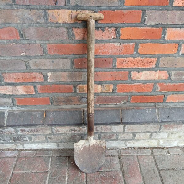 Vintage WWII military shovel against brick wall.
