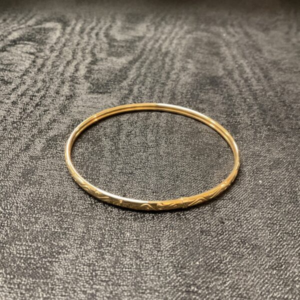 Delicate yellow metal bracelet with etched detailing.