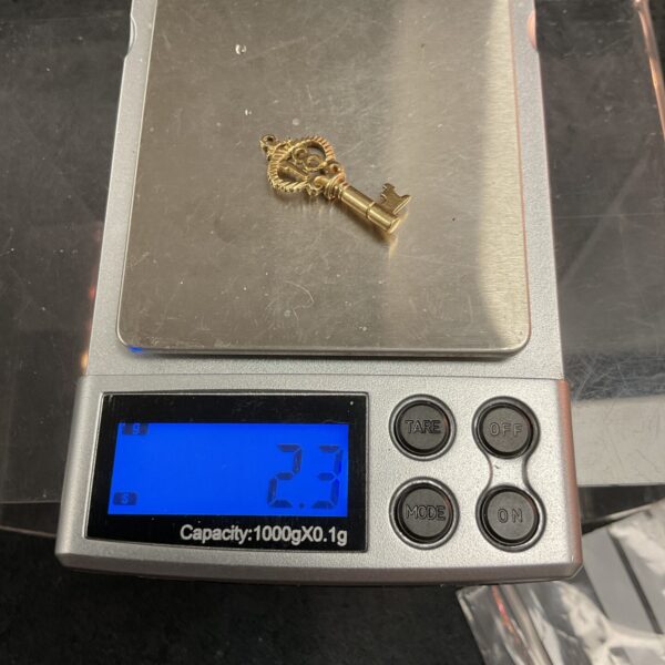 Close-up of a 9ct gold key charm with intricate detailing.