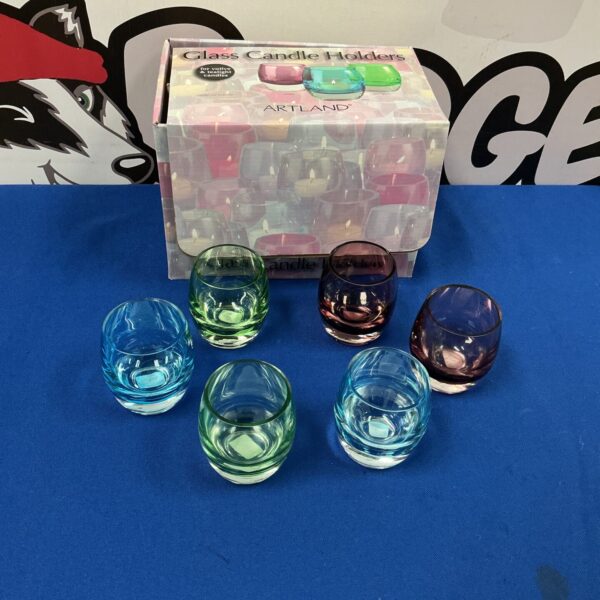 Assorted colourful Artland candle holders on a dark surface.