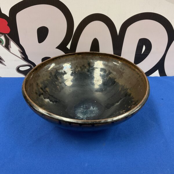 Dark black and brown glazed studio pottery bowl on blue surface.