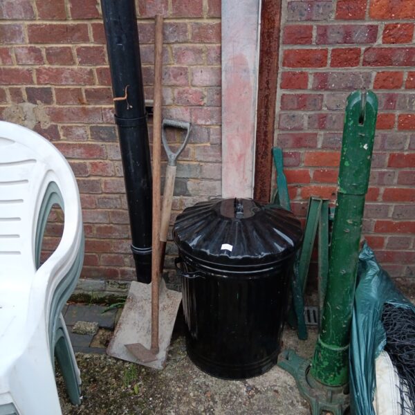 Black metal garden bin with shovel and hoe for outdoor use.