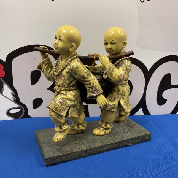 Detailed resin sculpture of Buddhist boys carrying water.