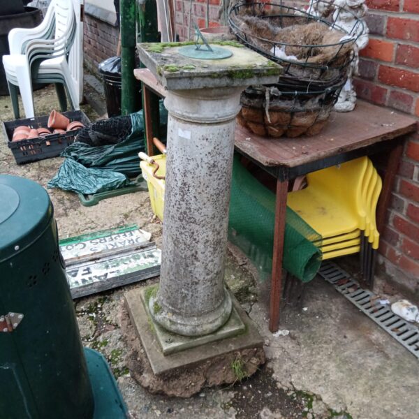 Weathered concrete sundial plinth in a garden setting.