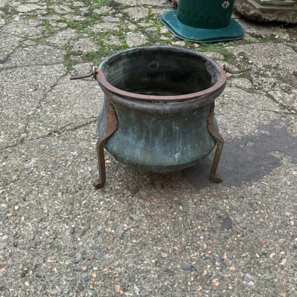 Antique copper cauldron with iron tripod base for garden or decor.