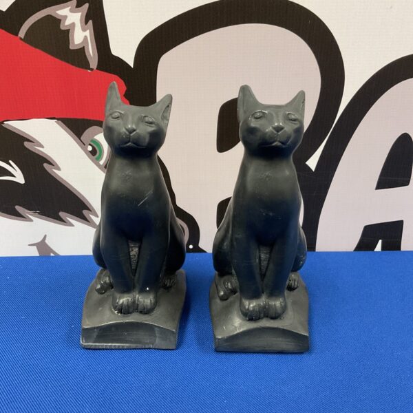 Pair of dark stone Egyptian cat statues on a white surface.