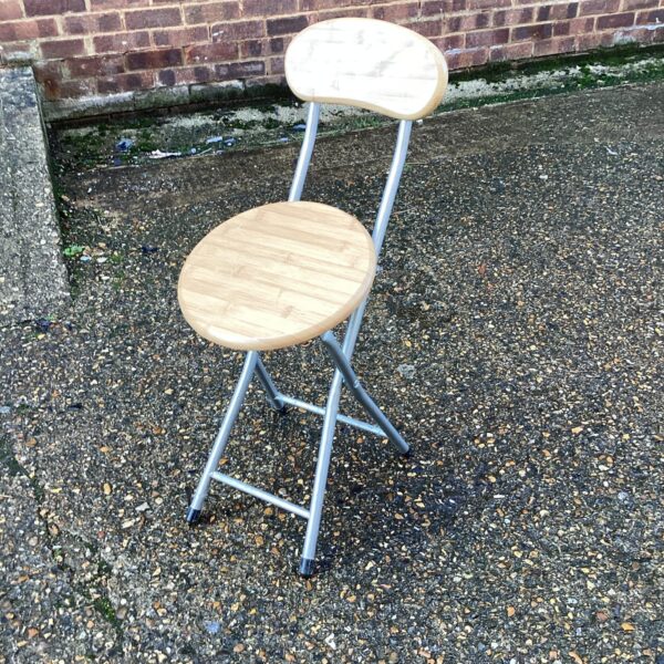 Side view of a folding kitchen stool with a circular seat.