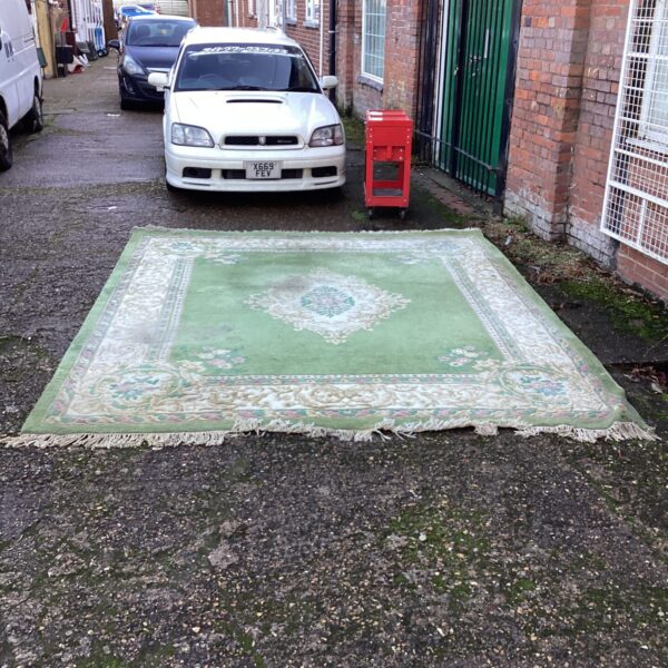 Large green floral rug displayed in a garden setting.