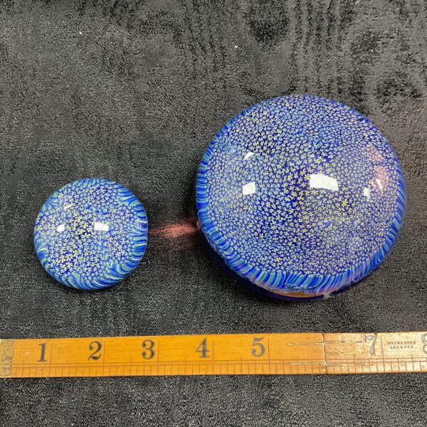 Pair of vibrant blue Murano millifiori paperweights on black surface.