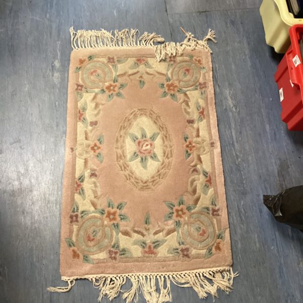 Small pink flower rug with fringed edges and floral pattern.