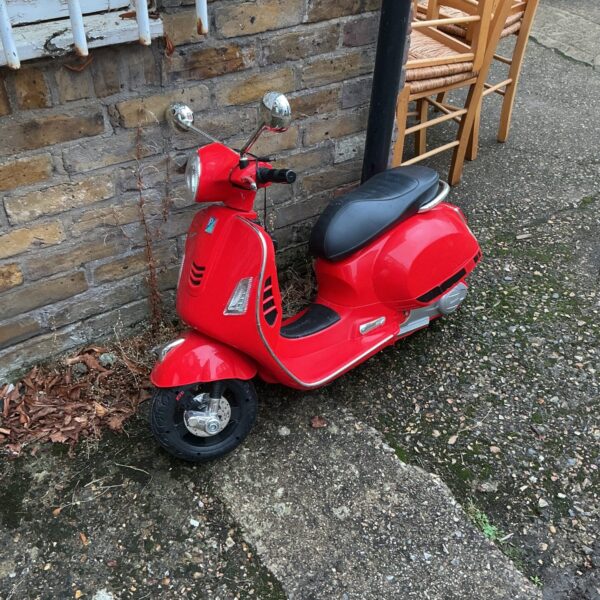 Red child’s battery powered scooter, side view.