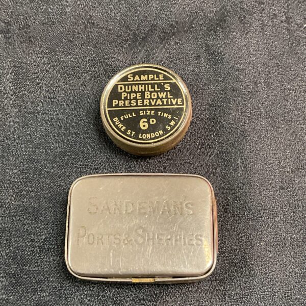 Vintage Sandemans vesta case and Dunhill tin on dark background.