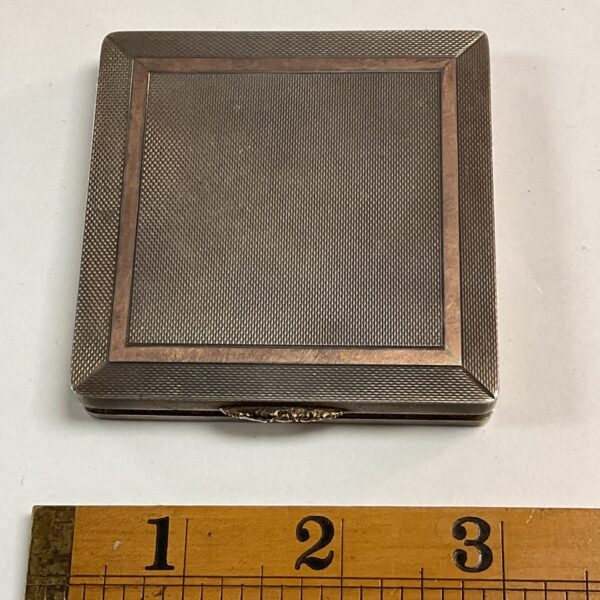 Silver art deco compact with textured geometric design.
