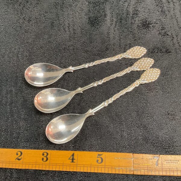Group of three antique silver coffee spoons with floral designs.