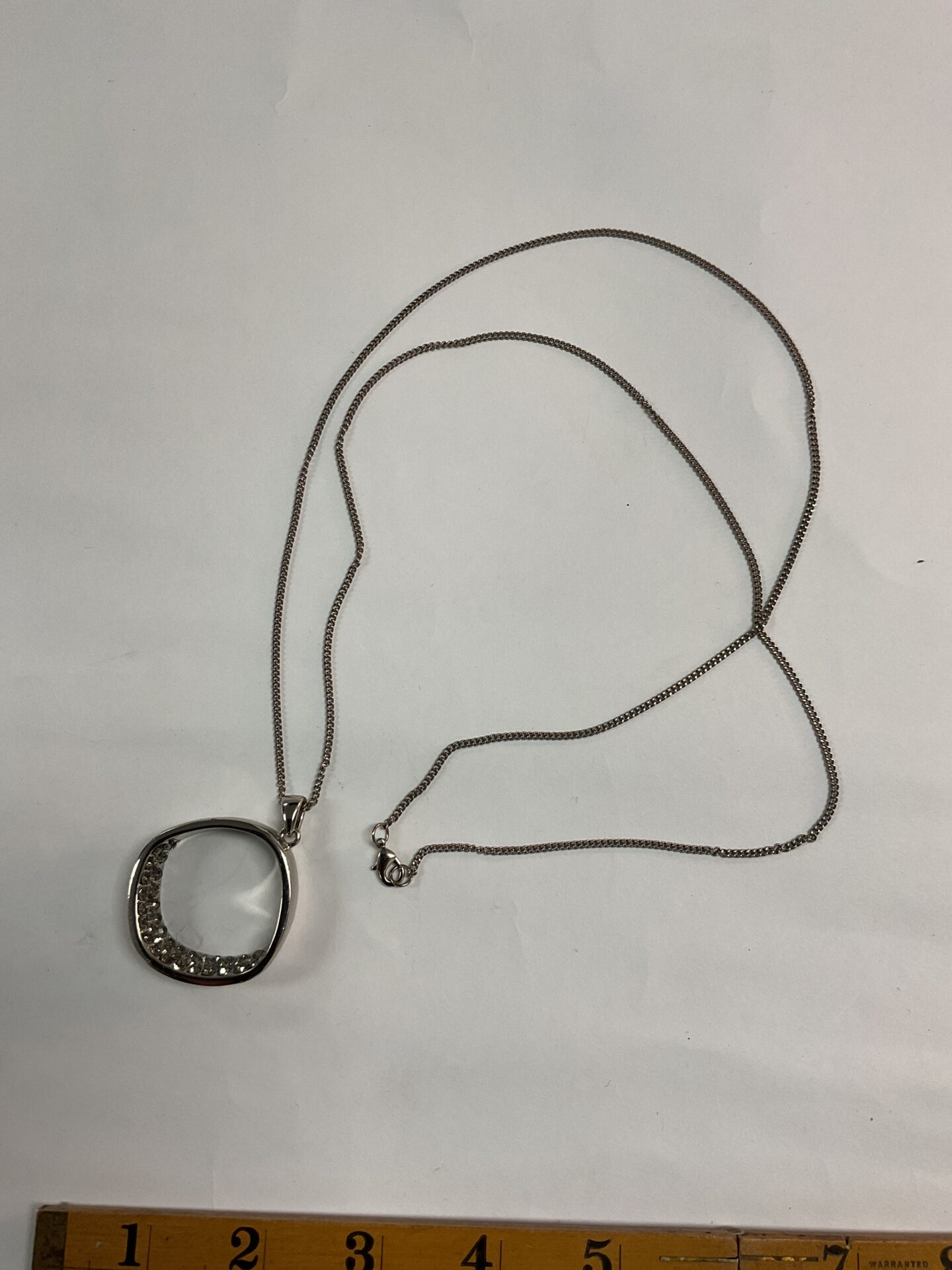 Silver tone necklace with large hoop pendant and clear stones.