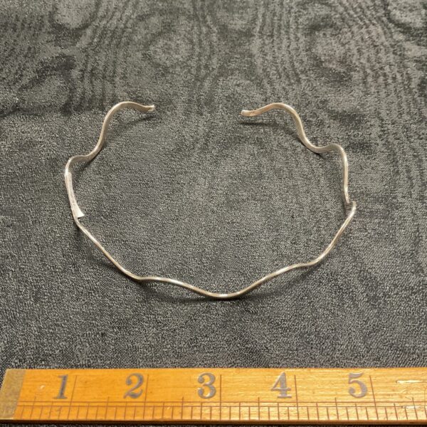 Close-up of a silver wavy choker necklace with a modern design.