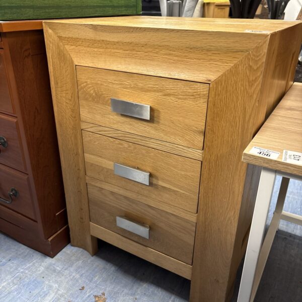 Solid oak three-drawer bedside cabinet for bedroom storage.
