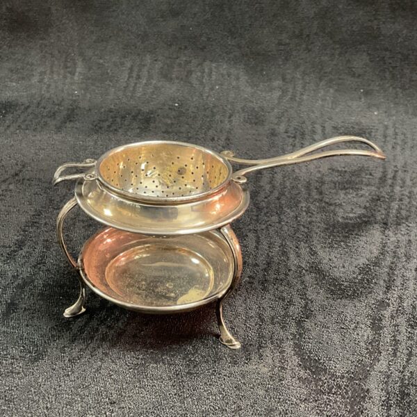 Vintage sterling silver tea strainer with stand on black background.