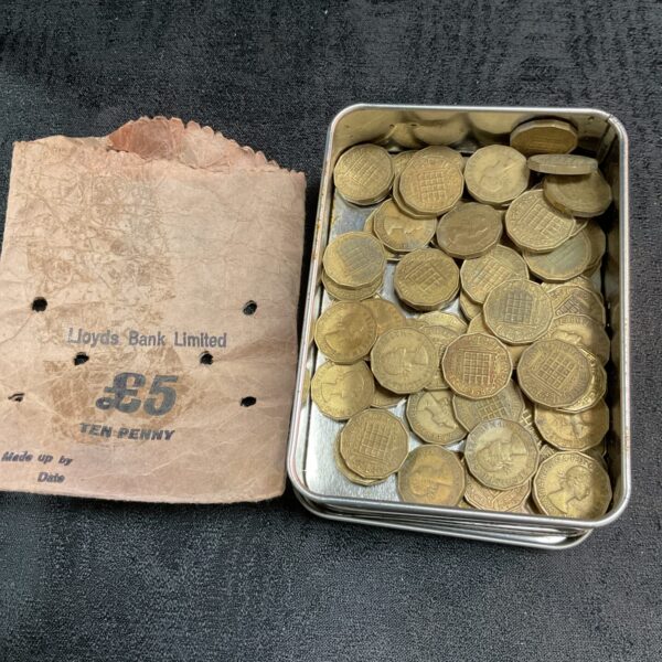 Vintage brass threepenny bits in a tin, British coin collection.