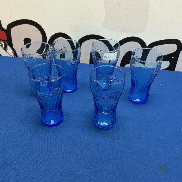 Six vintage Coca Cola glasses displayed on a patterned background.