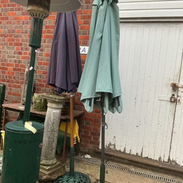 Two green vintage garden parasols with cast iron stands in a garden.