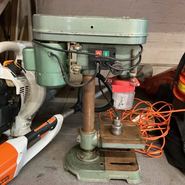 Front view of a vintage pillar drill in a workshop setting.