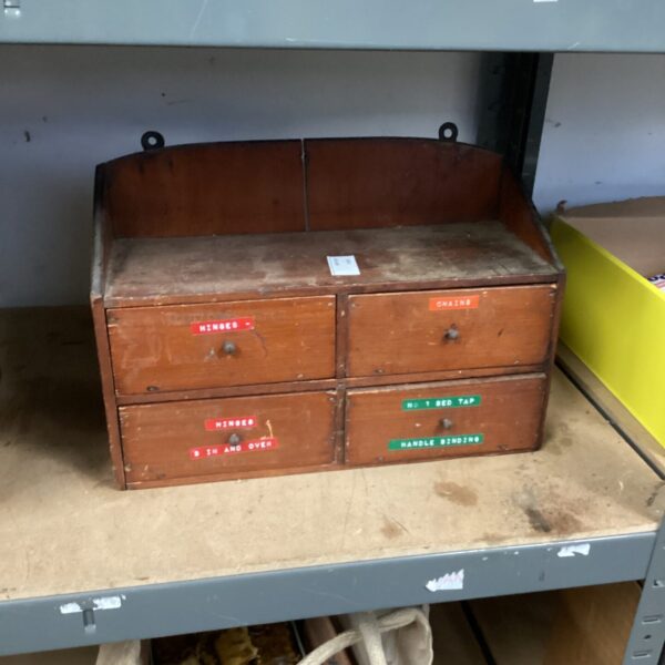 Front view of a vintage wooden tool cabinet with labelled drawers.