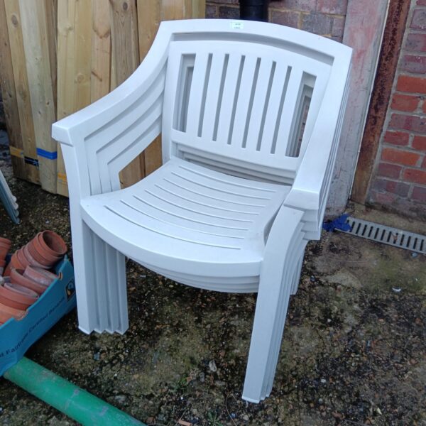 Set of four white plastic garden chairs stacked outdoors.