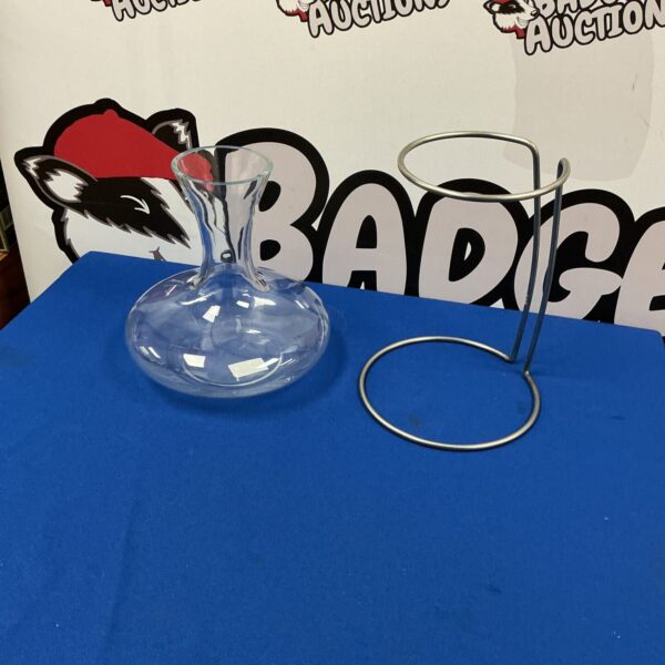 Clear glass wine carafe with metal holder for serving wine.