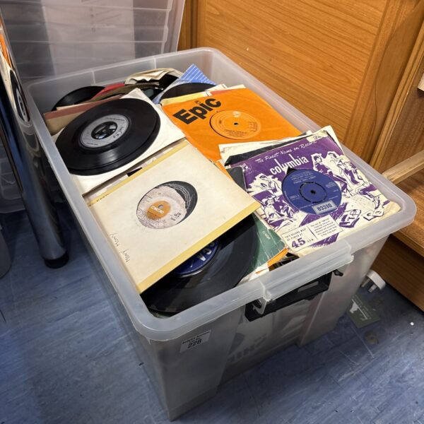 Large lot of mixed 7 inch vinyl singles in a storage container.