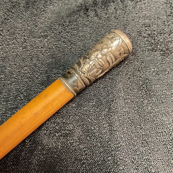 Close-up of antique malacca cane with detailed silver embossed top.