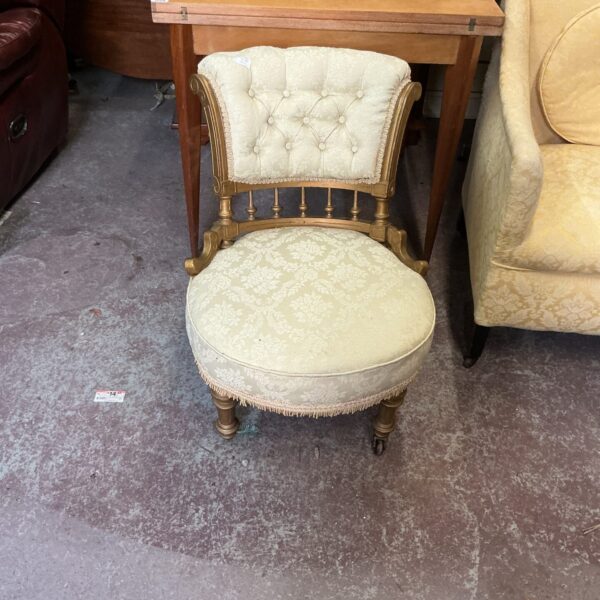 Cream upholstered antique nursery chair with carved wooden frame.