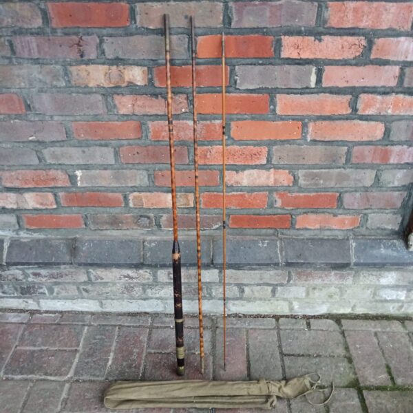 Antique tiger bamboo fishing rod displayed against brick wall.