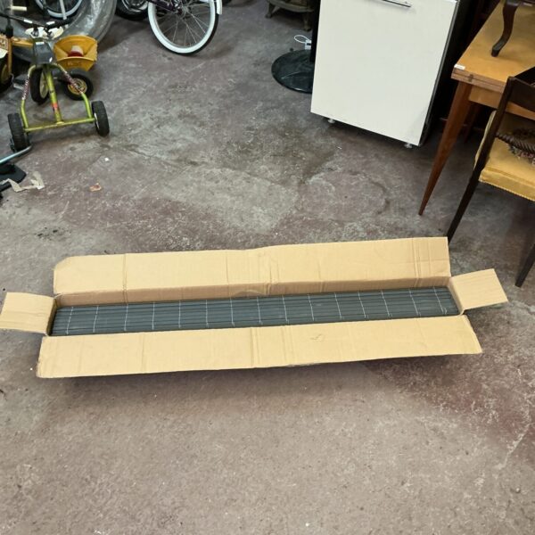 Grey window blind in original cardboard packaging.