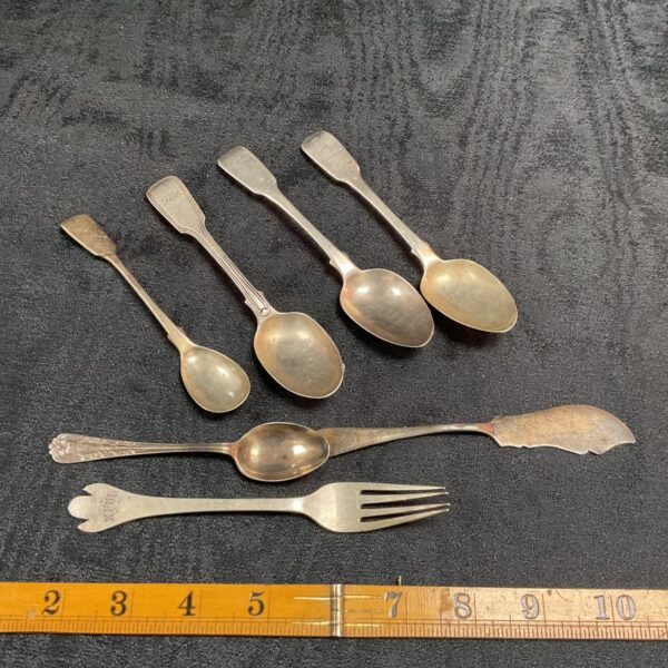 Group of antique hallmarked silver teaspoons on dark surface.