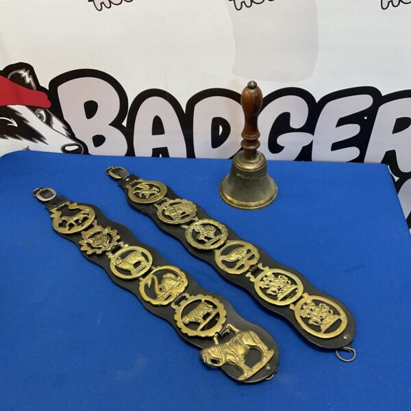 Antique horse brasses and hand bell on display.
