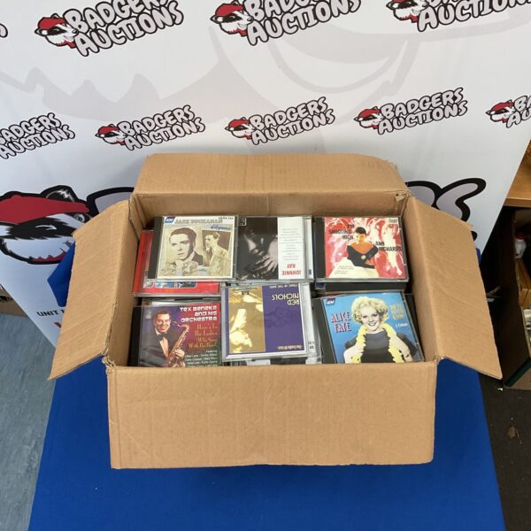 Mixed CD lot with various album covers in a cardboard box.