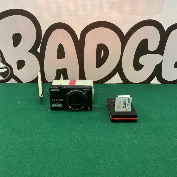 Black Nikon Coolpix S6100 digital camera on a green surface.