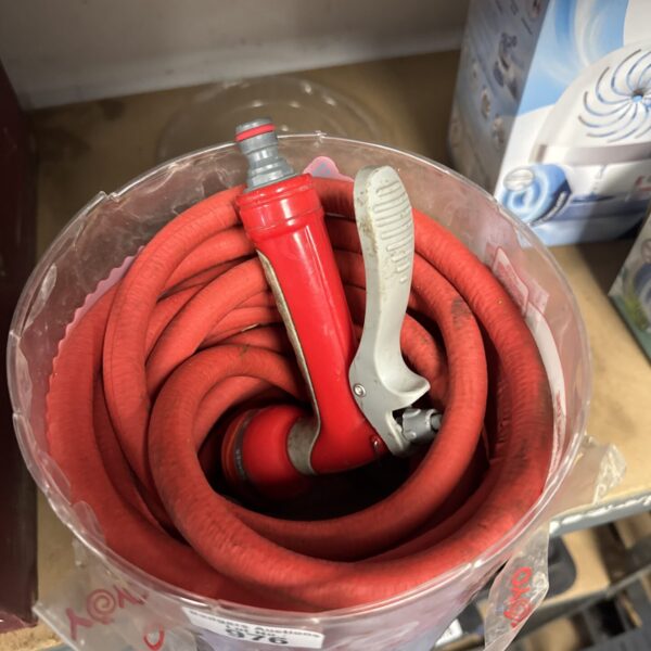 Red garden hosepipe with spray nozzle attachment for outdoor watering.