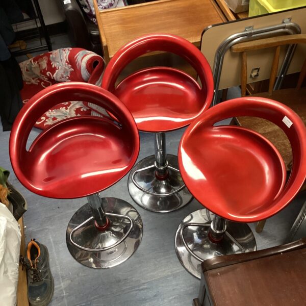 Three red height adjustable bar stools with chrome bases.