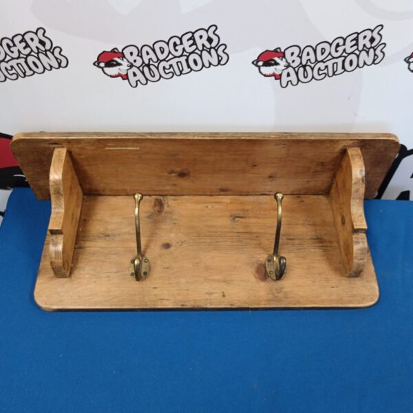 Rustic pine coat rack shelf with three hooks for hallway storage.