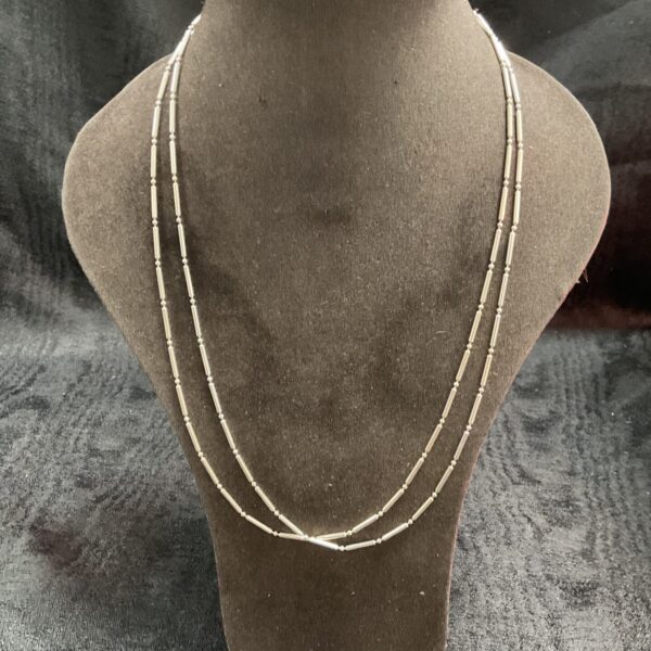 Two delicate silver bar link necklaces on a display.