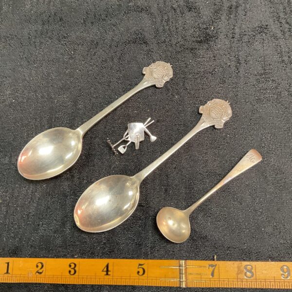 Antique silver golf spoons and mustard spoon on dark background.