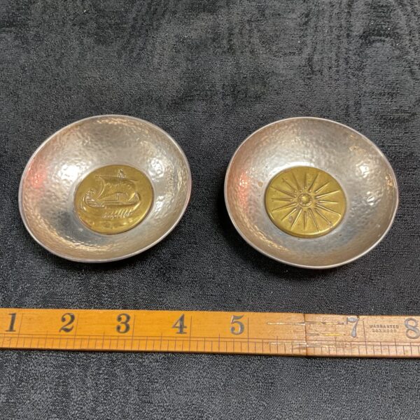 Close-up of a silver hand hammered dish with Viking ship brass centre.