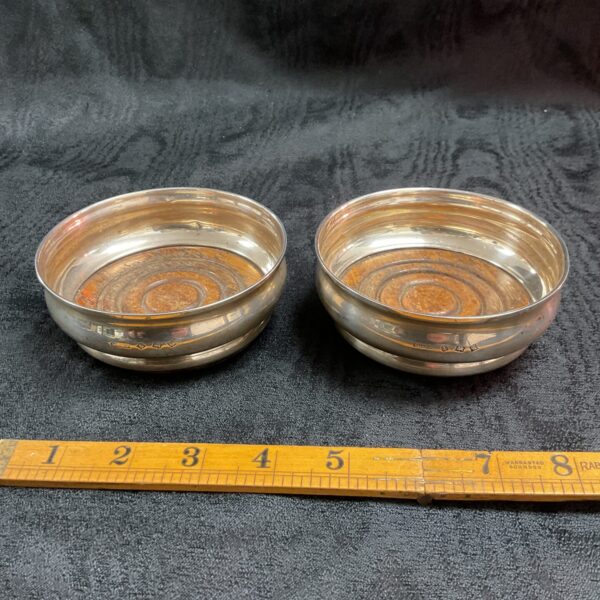 Pair of antique silver wine coasters on a dark surface.
